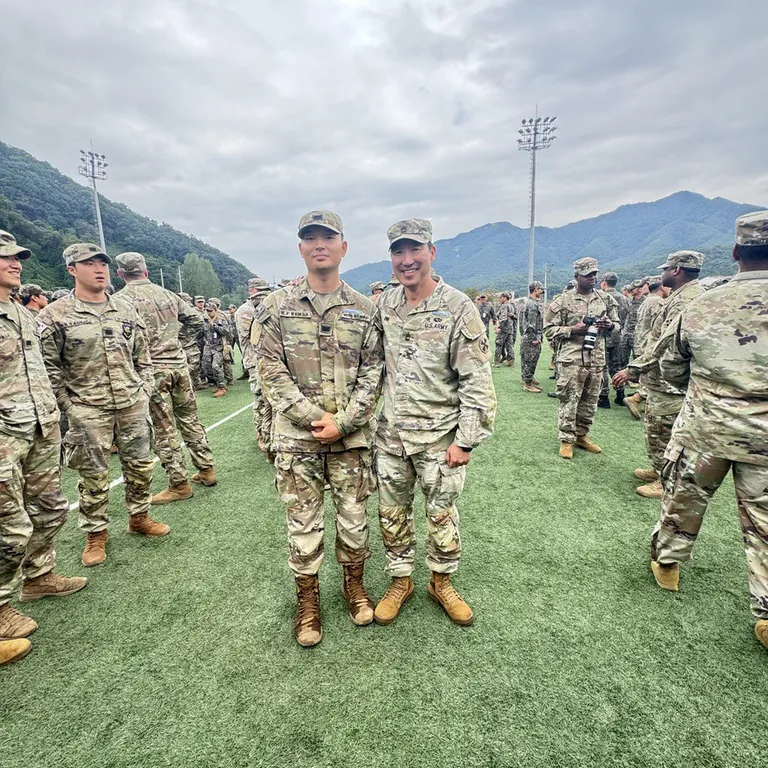 Doheon Kim and another soldier standing side by side on the field among other soldiers after the ceremony