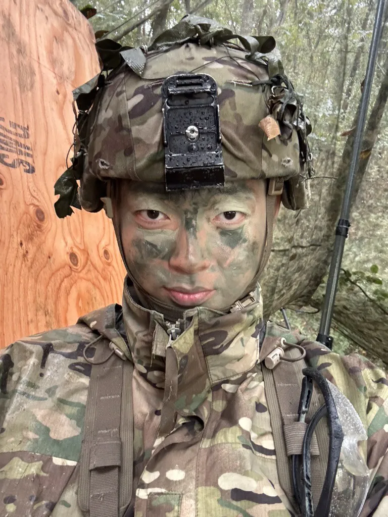 Close-up of Doheon Kim in camouflage face paint and a helmet covered in netting