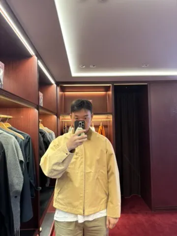 Doheon Kim taking a mirror selfie in a yellow jacket in a clothing shop