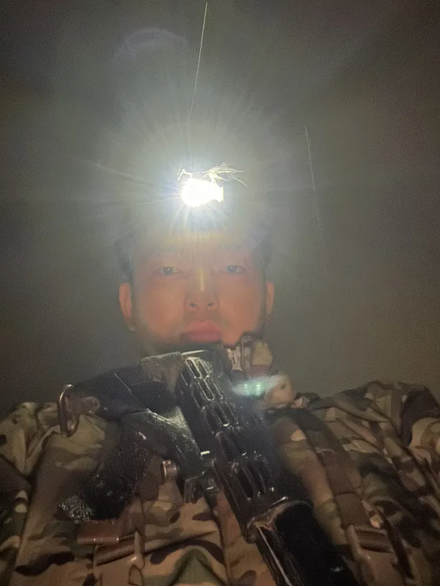Doheon Kim at night, lit only by the glare of his headlamp, holding his rifle
