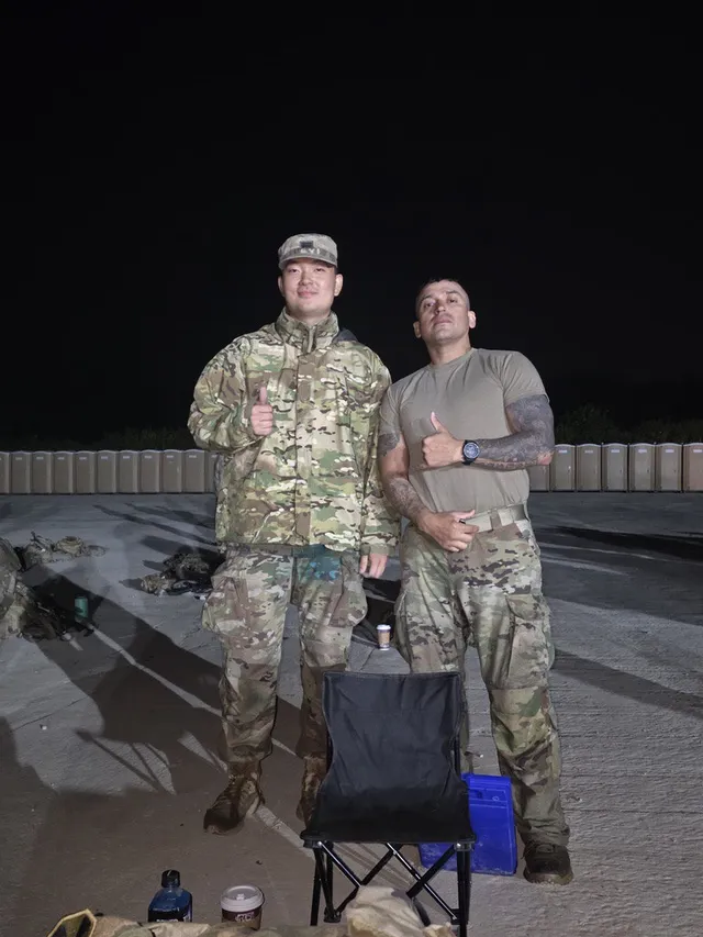 Doheon Kim and another soldier giving thumbs up at night beside a folding chair