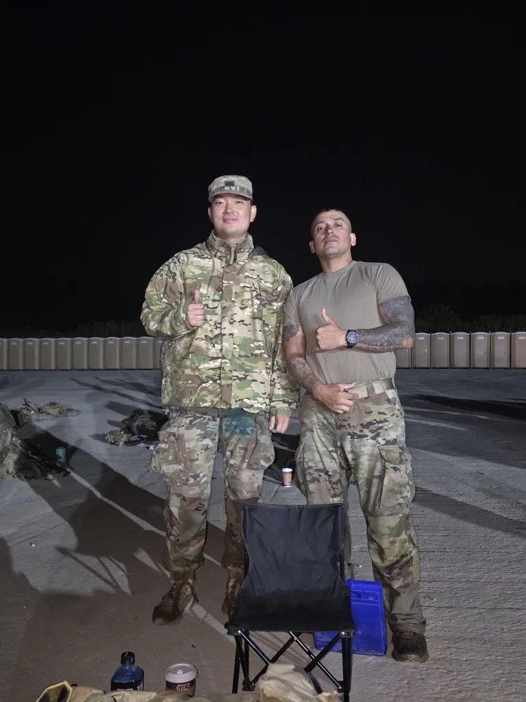 Doheon Kim and another soldier giving thumbs up at night beside a folding chair
