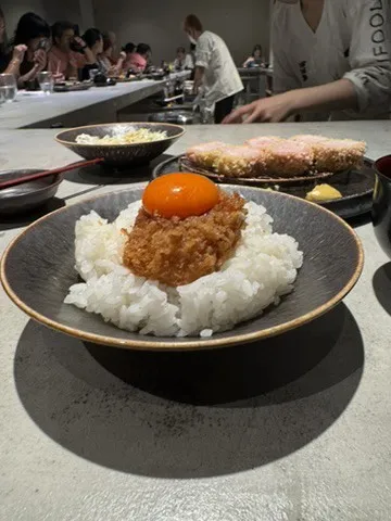 A bowl of rice topped with a minced cutlet and an egg yolk at a restaurant counter